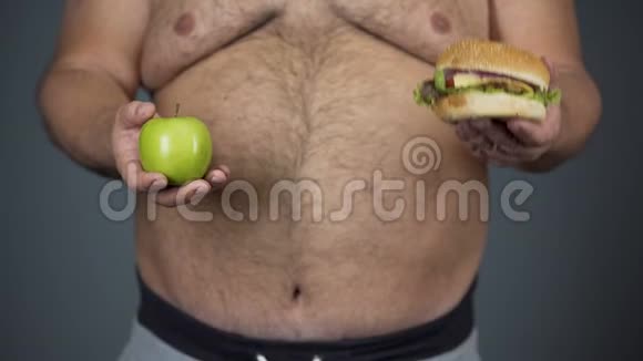 胖子选择苹果而不是汉堡包保持健康的饮食腹部特写视频的预览图