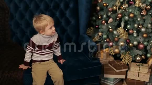 男孩坐在圣诞树附近的沙发上视频的预览图