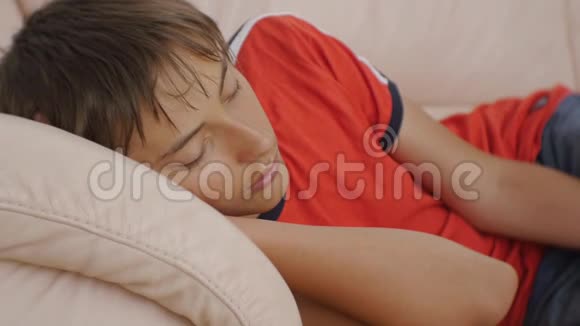 年轻人睡在沙发上穿红色t恤和蓝色牛仔裤睡在米色皮革沙发上的白种人少年特写视频的预览图