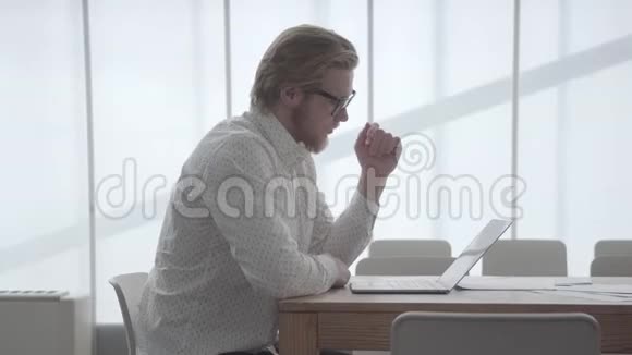 肖像英俊的金发体贴的商人戴着眼镜坐在桌子前在一间舒适的办公室前视频的预览图