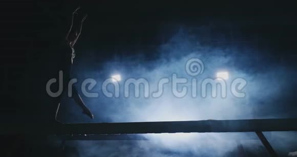 这个女孩在一个背光的日志上表演一个技巧在运动体操服装中表演慢动作烟和蓝色跳跃和跳跃视频的预览图
