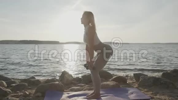 年轻的运动美女手里拿着哑铃在大海的背景上健身女孩做运动视频的预览图