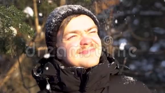 在冬天的森林里留着小胡子小胡子面带笑容的年轻男子欣赏着降雪的从灿烂的阳光中眯起眼睛视频的预览图