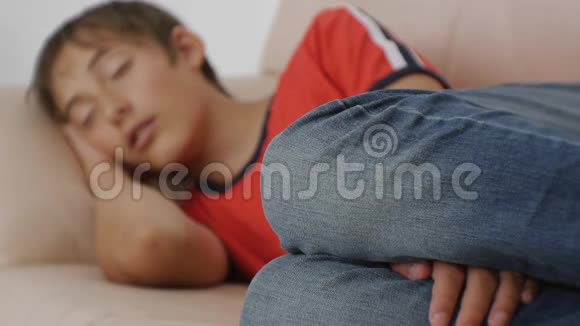 年轻人睡在沙发上穿着红色t恤和蓝色牛仔裤睡在米色上的白种人少年的焦点镜头视频的预览图