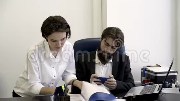 女士办公室工作人员向她那长胡子的老板出示重要文件老板正忙着在办公室玩智能手机游戏视频的预览图