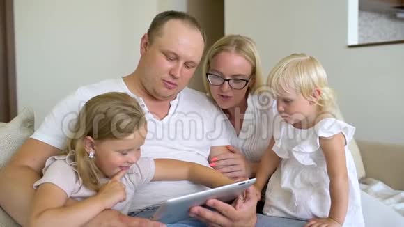 快乐的家庭一起玩笔记本电脑和数字平板电脑在家里爸爸妈妈和两个孩子坐在沙发上视频的预览图