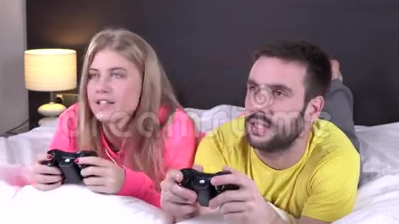 可爱的年轻夫妇在床上玩电子游戏视频的预览图