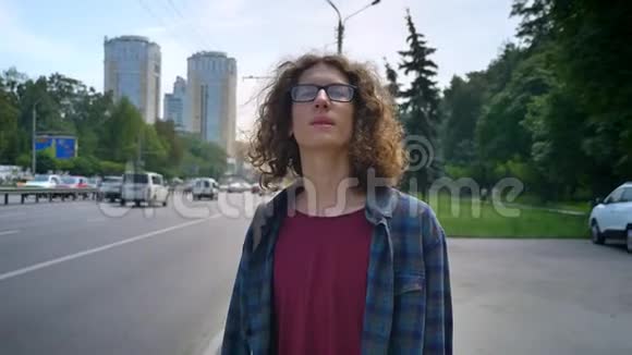 年轻的帅哥戴着眼镜留着长长的波浪发等待出租车或公共汽车向前看站在城市的街道上视频的预览图