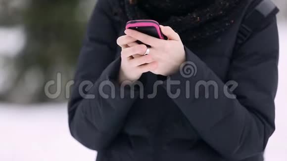 一个戴着眼镜戴着红色针织帽子的漂亮女孩的手用智能手机获取一条短信视频的预览图