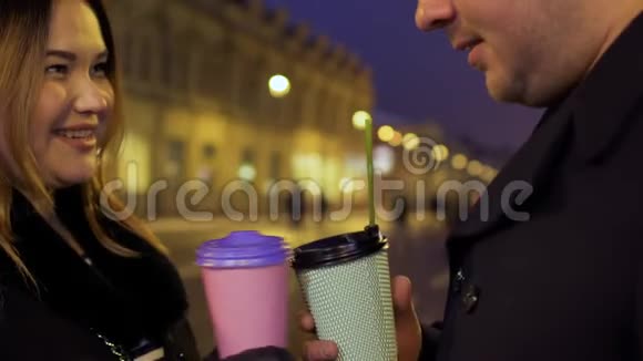 这对年轻夫妇在夜晚聊天喝咖啡照亮街道背景视频的预览图