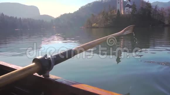 在阳光明媚的一天一只桨在水中划桨在背景中划桨的岛屿湖斯洛文尼亚的布莱德湖视频的预览图