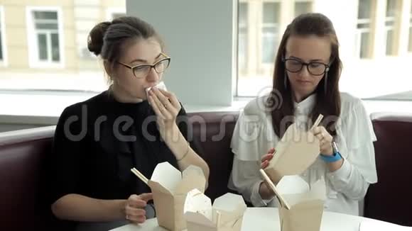 两个戴眼镜的女商人坐在咖啡馆里午餐吃中国面条食物咖啡上班休息视频的预览图