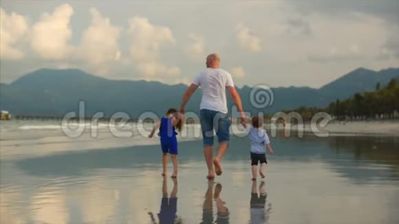 年轻的家庭一个父亲和他的儿子和女儿沿着海岸在海岸上散步幸福的家庭散步视频的预览图