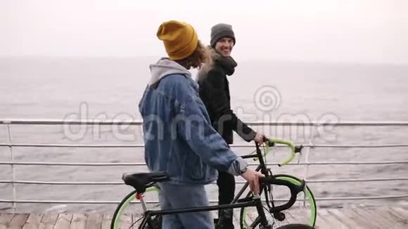 美丽的微笑的一对年轻的嬉皮士在秋日和他们的自行车一起在海边散步走过去视频的预览图