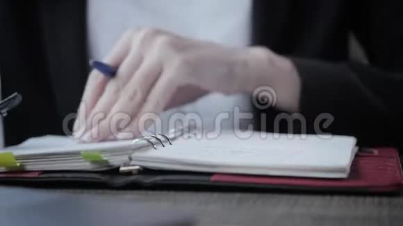 女人在笔记本上做笔记的特写年轻的女商人坐在木桌旁的咖啡店里关于视频的预览图