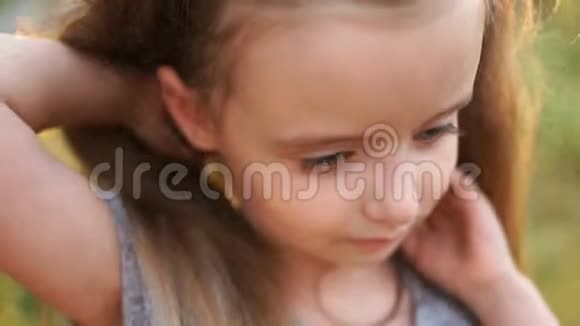 一位留着长发和灰色眼睛的漂亮小女孩的精彩亲密肖像在一个夏天的背景下视频的预览图