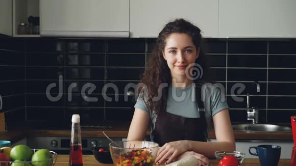 年轻的白种人行政厨师的肖像穿着围裙坐在现代轻盈宽敞的厨房里的餐桌上微笑着视频的预览图