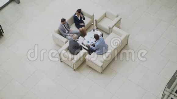 一群商务人士同事坐在大厅的沙发上讨论金融图表的全景照片视频的预览图