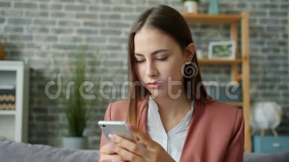 漂亮的女孩用现代智能手机触摸屏幕在家微笑视频的预览图