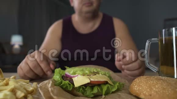 暴饮暴食肥胖男人做大汉堡美食家欣赏他的饭菜特写视频的预览图