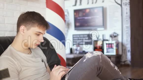 年轻人用平板电脑在理发店等待轮到他视频的预览图