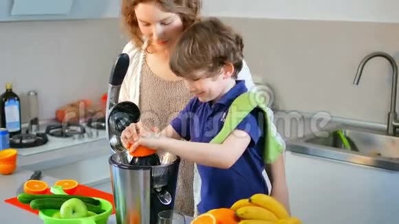 年轻的白种人母亲和孩子在厨房用电榨汁机制作鲜橙果汁视频的预览图