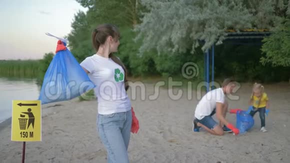 清洁海滩年轻志愿者母亲戴着橡胶手套的肖像背景上的指针标志附近有垃圾袋视频的预览图