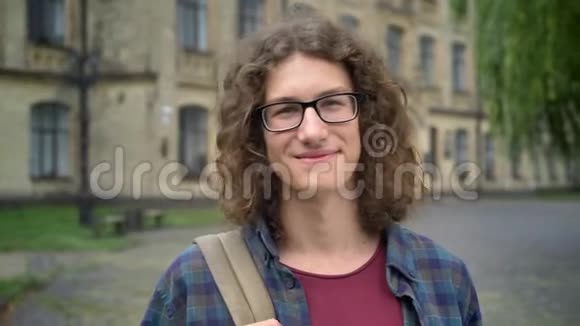 年轻英俊的快乐学生戴着眼镜和背包站在大学校园附近的街道上微笑着视频的预览图