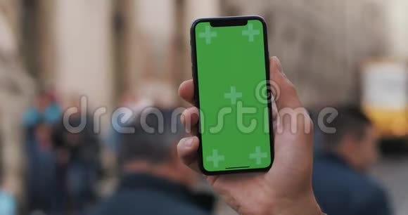 特写一个男人手拿着一部移动电话街道上有一个垂直的绿色屏幕视频的预览图