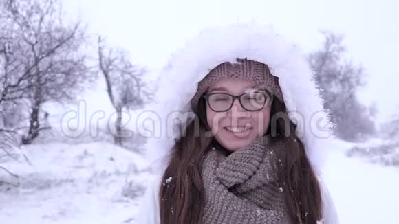 微笑的女孩戴着眼镜站在雪花飞舞的大自然中视频的预览图