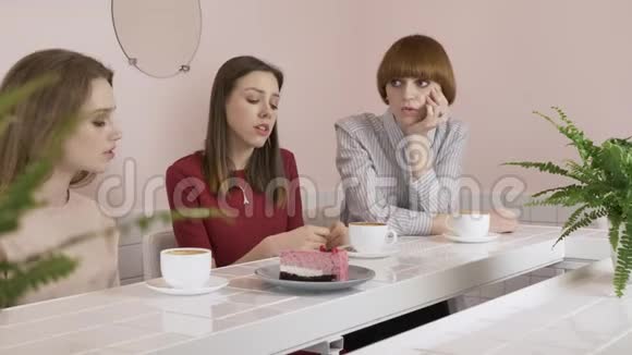 三个年轻的白人女孩坐在咖啡馆里喝咖啡吃蛋糕悲伤用手打手势八卦视频的预览图