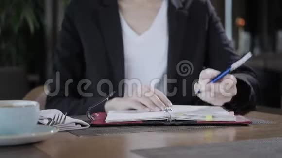 女人在笔记本上做笔记的特写年轻的女商人坐在木桌旁的咖啡店里视频的预览图