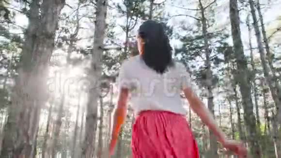 一个年轻漂亮的女人正高兴地在树林里的许多松树之间奔跑从后面看视频的预览图