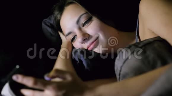 女孩晚上躺在卧室的床上上网看照片聊天和微笑视频的预览图
