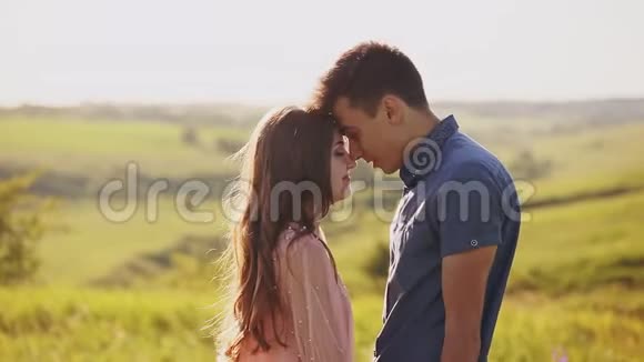 一对年轻漂亮的夫妇拥抱亲吻日落时的自然田野视频的预览图