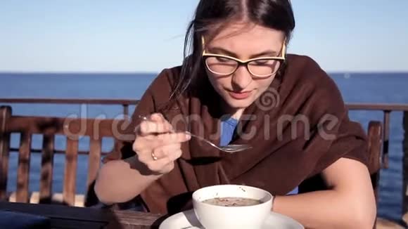 傍晚日落时分一个女孩坐在一家俯瞰大海的咖啡馆里铺着毯子吃热汤视频的预览图