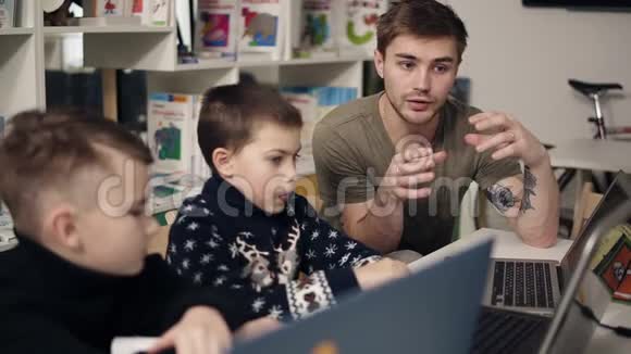 年轻迷人的男程序员老师正在向他的两个小家伙解释一些关于技术和计算机的事情视频的预览图