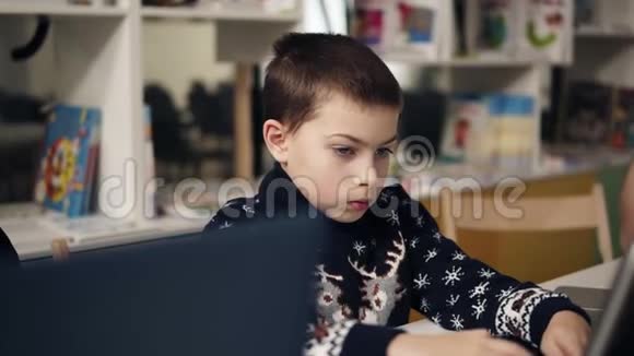 一个小男孩坐在笔记本电脑屏幕前的蓝色大眼睛肖像的慢镜头编程课视频的预览图
