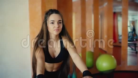 一个头发长长的漂亮黑发女孩在健身房骑自行车视频的预览图