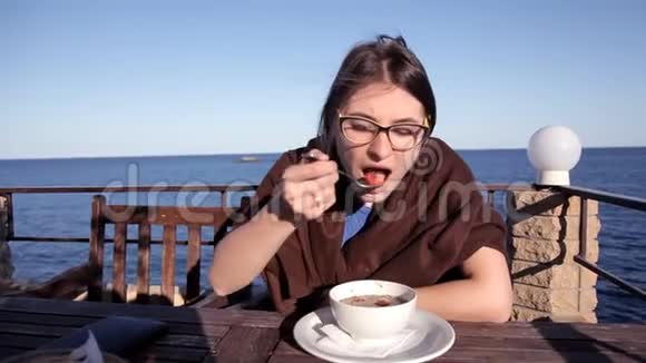 傍晚日落时分一个女孩坐在一家俯瞰大海的咖啡馆里铺着毯子吃热汤视频的预览图