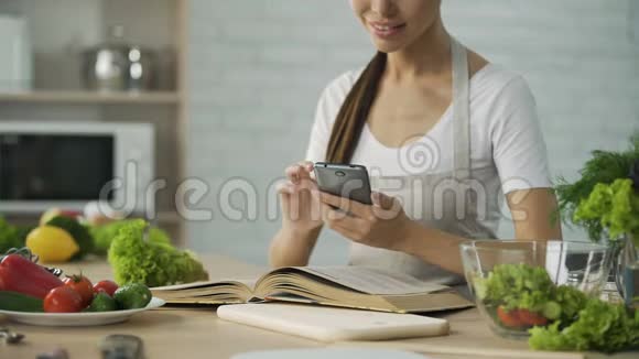 漂亮的女人在看烹饪书计算智能手机应用程序的卡路里视频的预览图