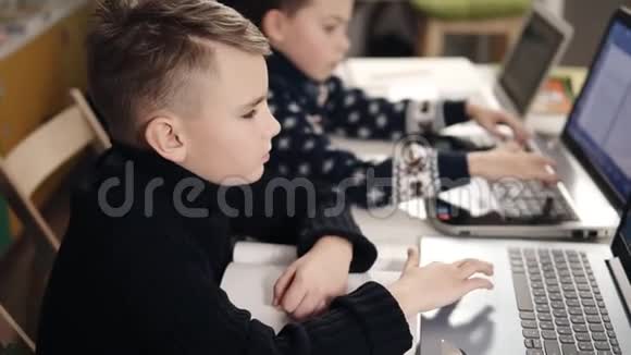 两个小男孩坐在他们的笔记本电脑前学习如何编程视频的预览图