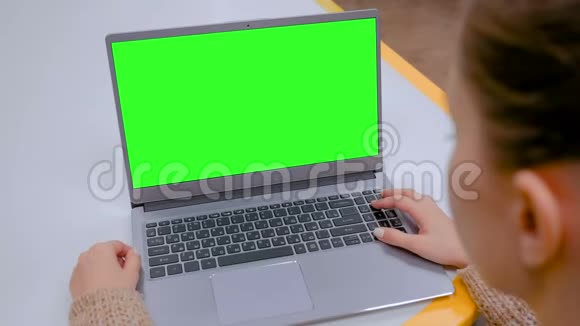女人在咖啡馆里看着一台绿色屏幕空白的笔记本电脑视频的预览图