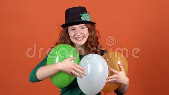庆祝圣帕特里克节的年轻女子戴着帽子在橙色墙上玩气球视频的预览图