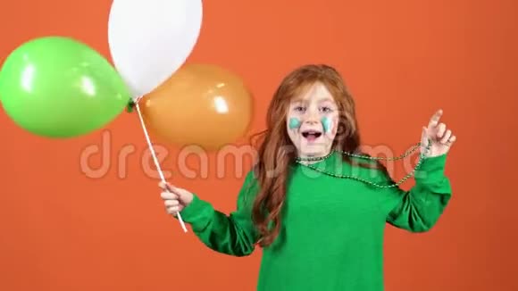 庆祝圣帕特里克节的女孩红发橙色背景手捧蝴蝶结玩珠子视频的预览图