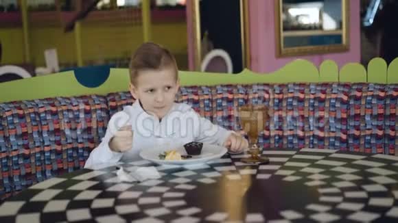 英俊的微笑男孩吃着美味的甜点在咖啡馆里点头视频的预览图