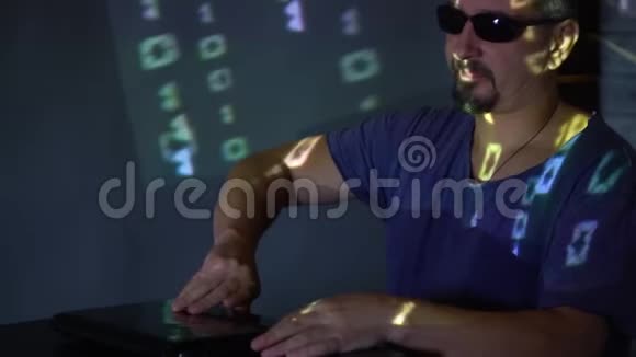 一个戴太阳镜的黑客在黑暗的房间里使用程序代码网上犯罪概念视频的预览图