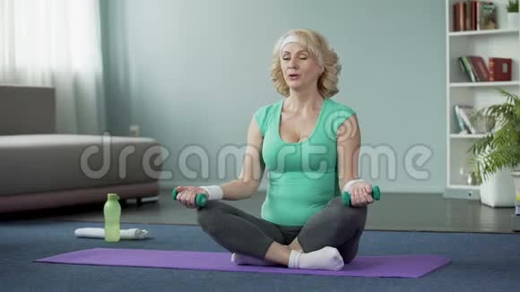 漂亮的老太太坐在地板上举起哑铃锻炼身体视频的预览图