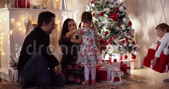 快乐的父母用装饰好的树把圣诞礼物送给他们的孩子视频的预览图