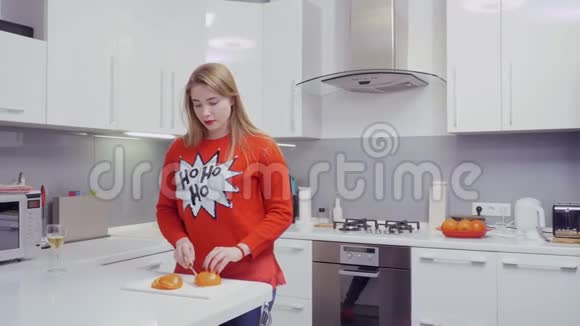 穿红色毛衣的漂亮女孩在厨房切柿子吃水果视频的预览图